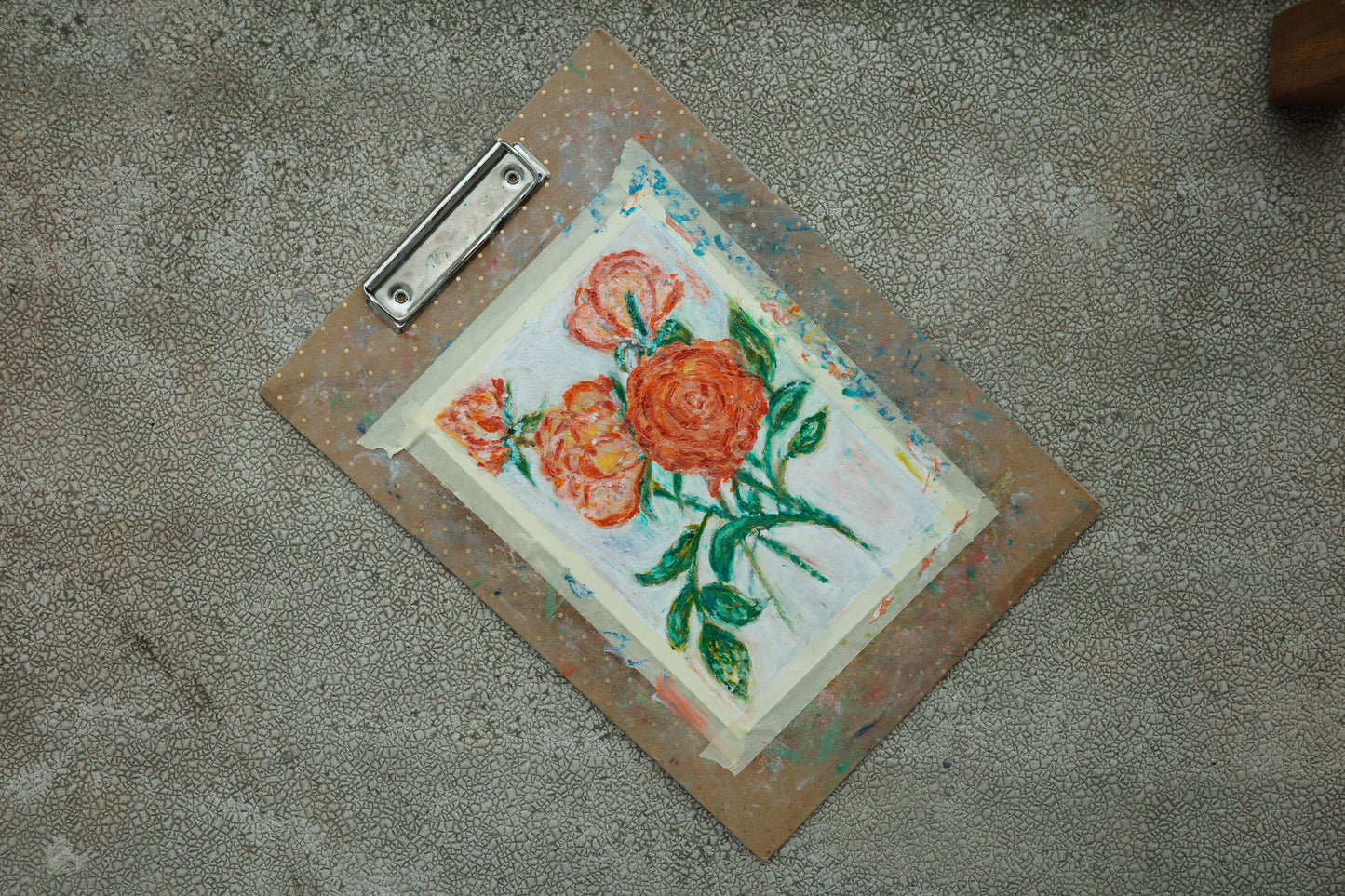 Artistic depiction of flowers on a piece of paper held by a clipboard on a concrete surface.